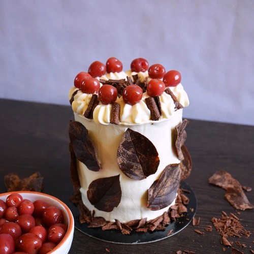 Foto de una torta Selva Negra, decorada con chocolate en forma de hojas alrededor y arriba decorada con picos de chantilly, cerezas y trozos de choclate